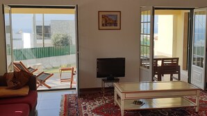 A living room with a sofa, a TV, a coffee table, and a chessboard. There are two doors leading to outdoor areas. - Harmonic House with sea view (Atalaia Lourinhã)