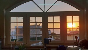 A kitchen with a large arched window overlooking a sunset, a sink, and various kitchen items. - Harmonic House with sea view (Atalaia Lourinhã)