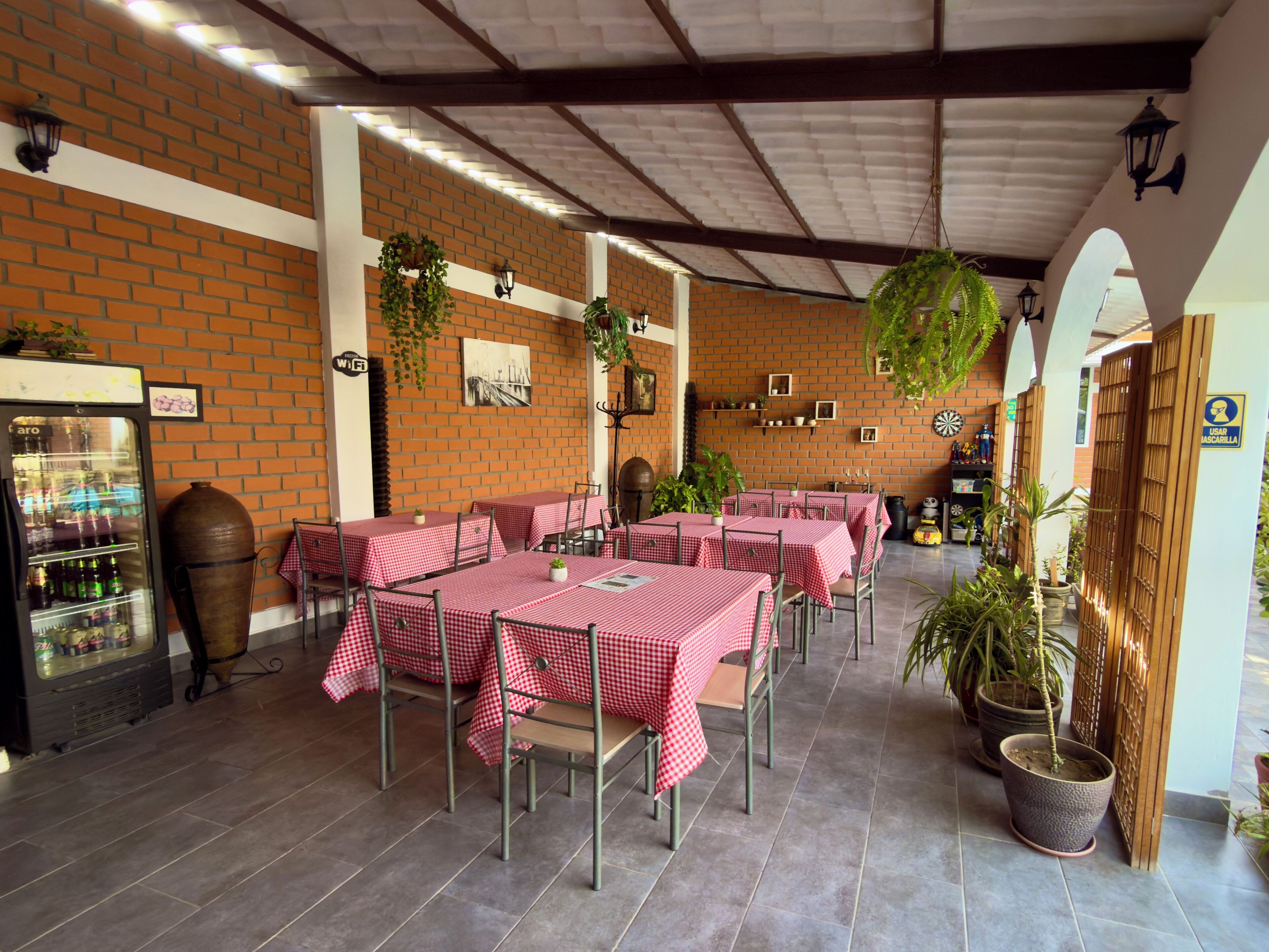 A restaurant with brick walls, red checkered tables, and hanging plants.