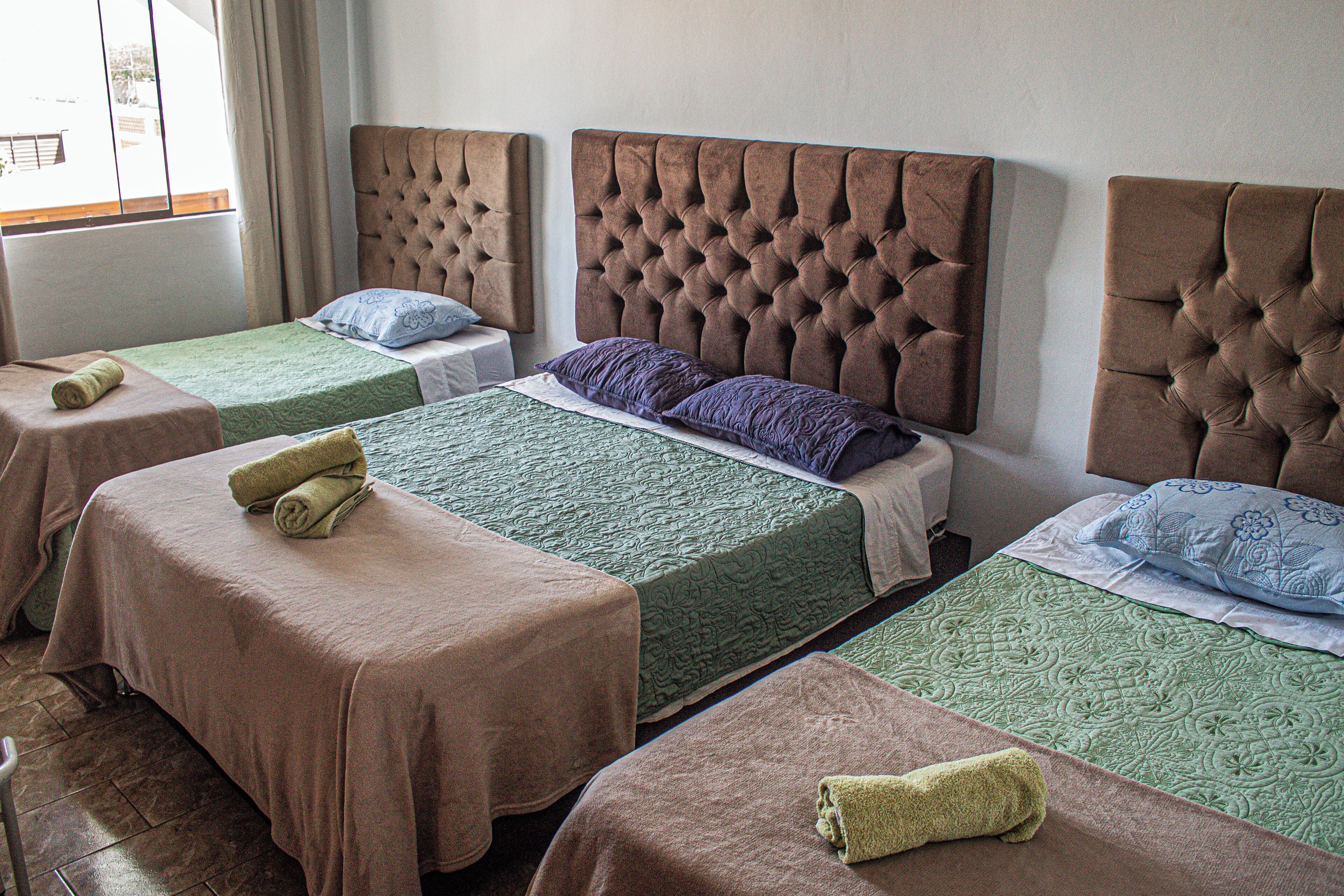 A hotel room with four beds, each with a different colored bedspread and matching pillows.
