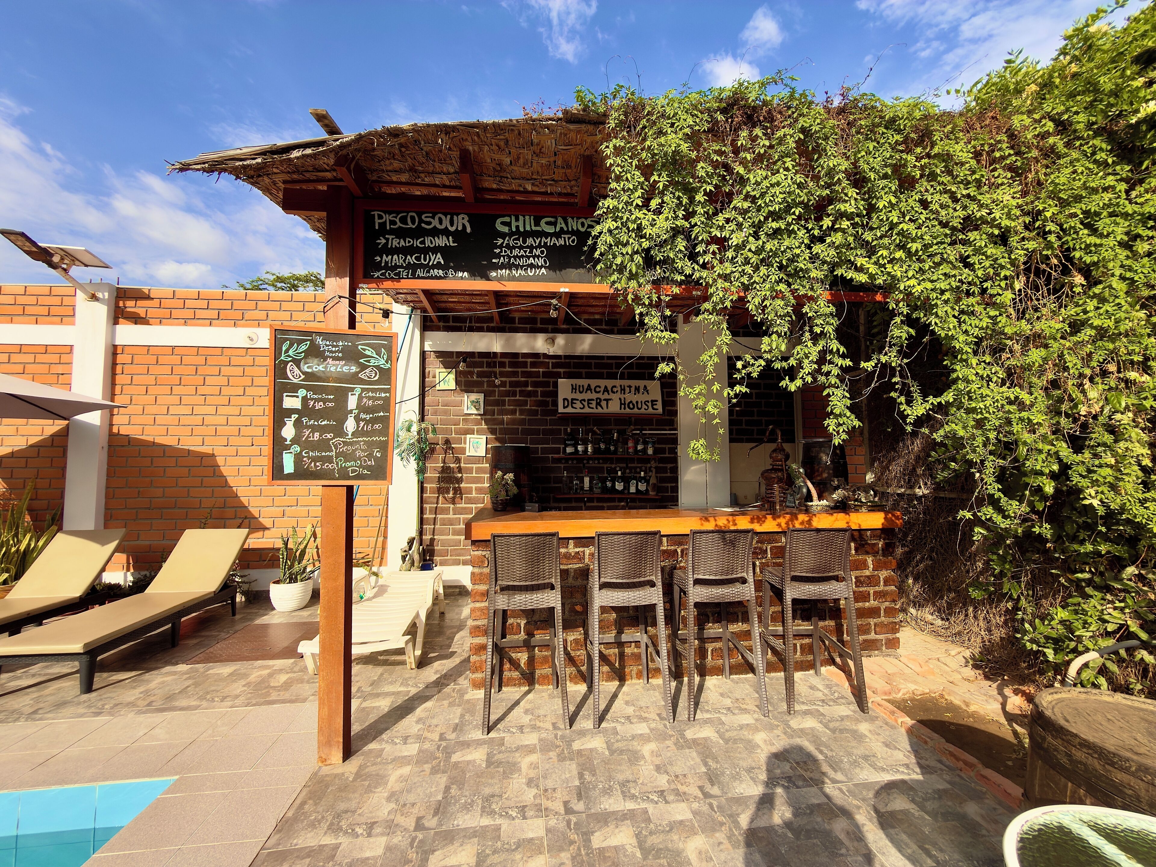 Een buitengebied met een bar, een menubord en een bordje voor Huacachina Dessert House.