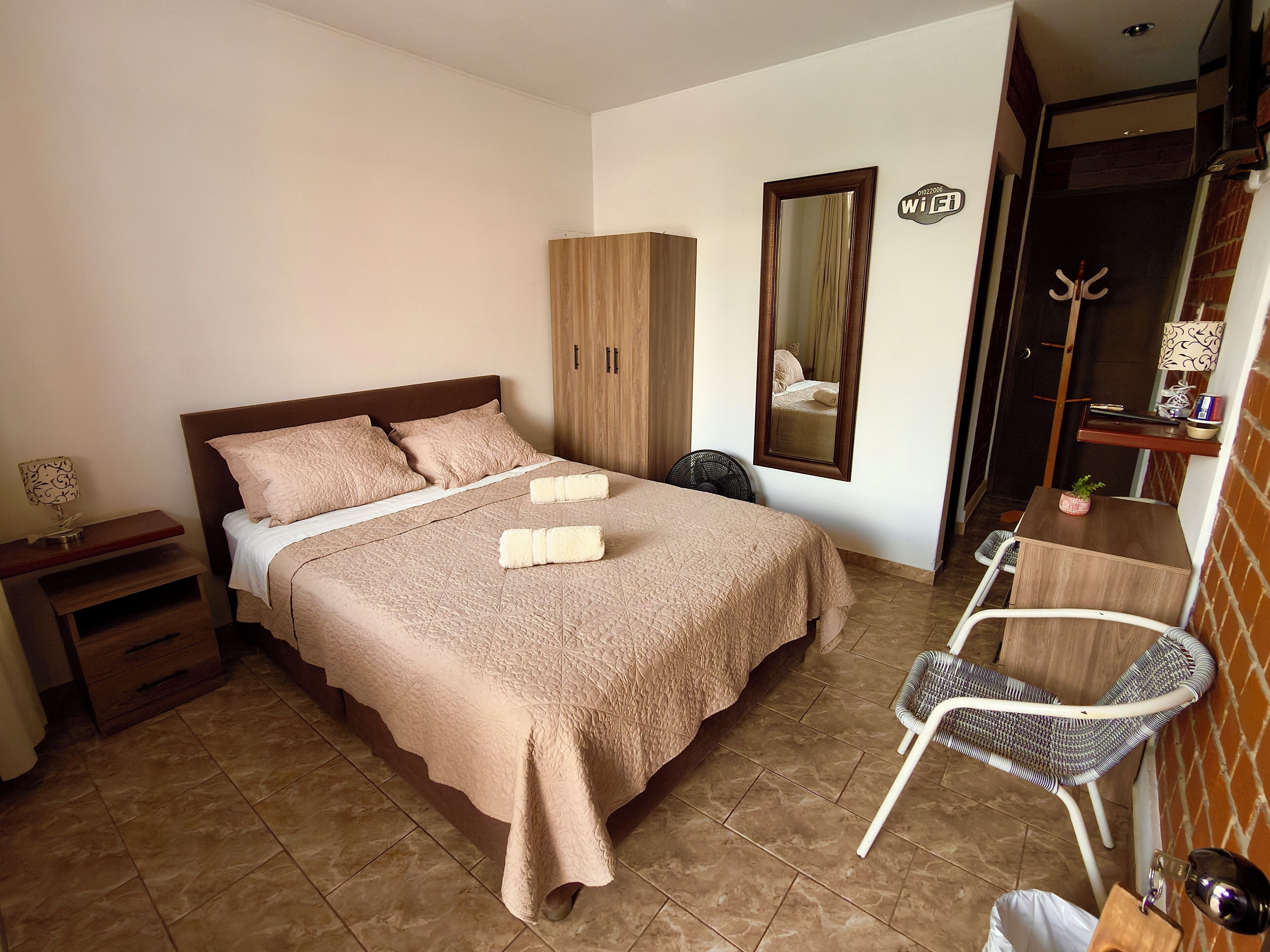 A neatly arranged bedroom with a bed, bedside tables, a chair, a wardrobe, a mirror, and a small table with a lamp.