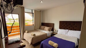 A hotel room with two beds, a desk with a computer, a small plant, and a window with curtains.