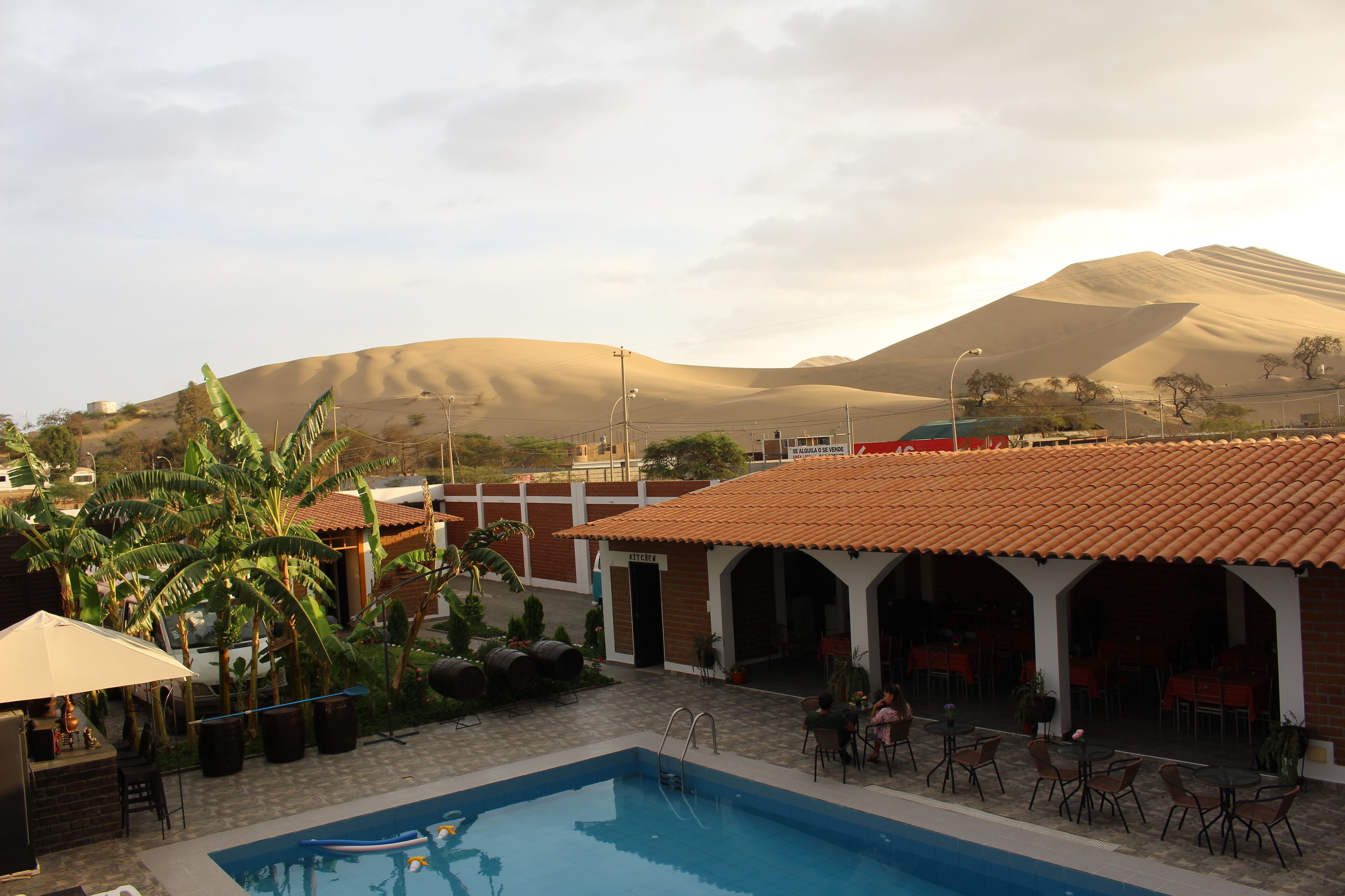 Zona de piscina con vistas a dunas de arena y un edificio con tejado de tejas.