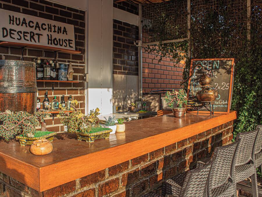 Zona de bar con un letrero que dice "HUACACHINA DESERT HOUSE" y una pizarra publicitaria que anuncia "OPEN BAR 2x25".