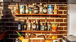 A bar area with a sign reading "Huacachina Desert House" above a shelf of various bottles. Two drinks are on the bar counter.