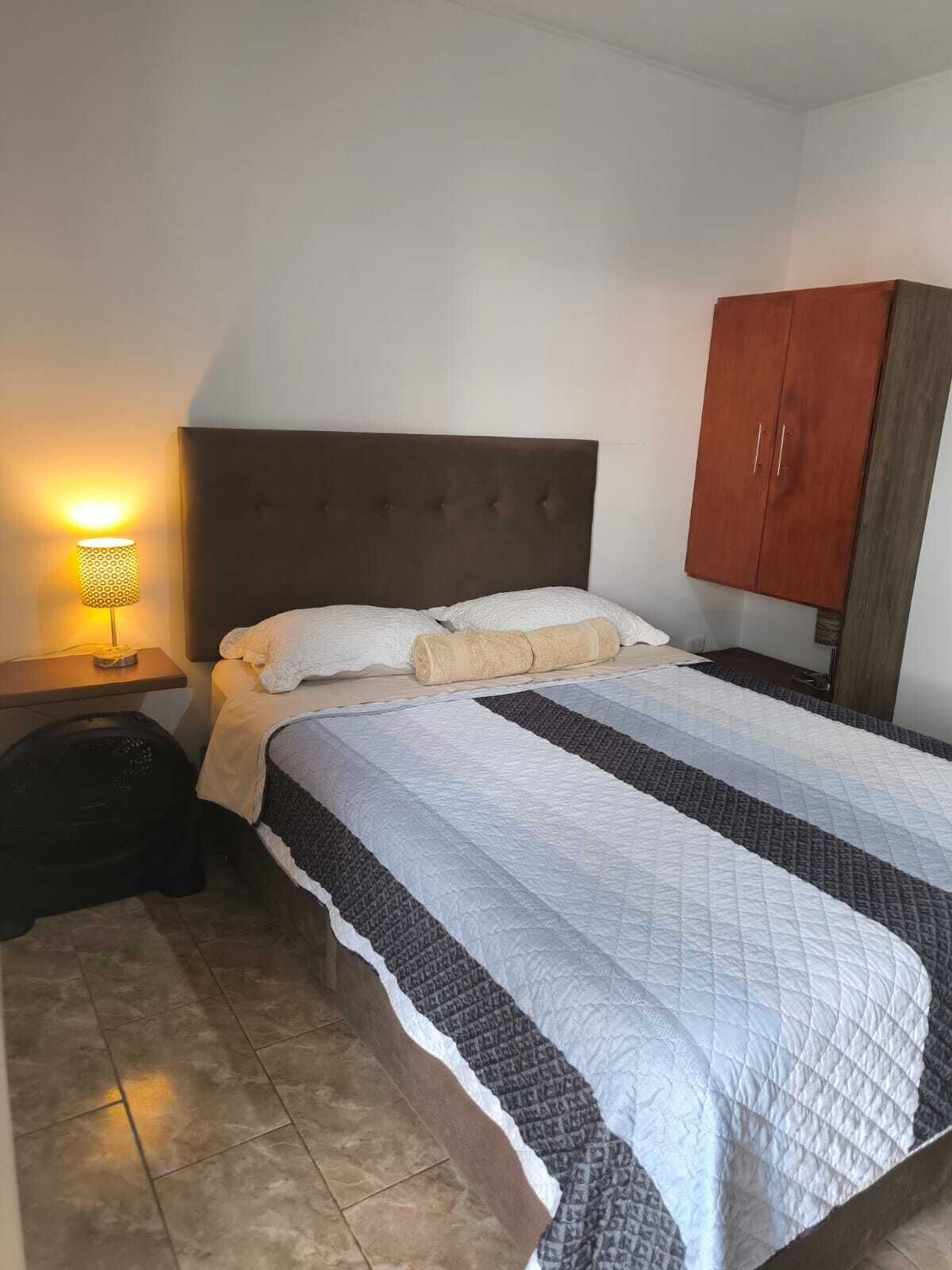 Un dormitorio con una cama, una mesita de noche, una lámpara y un armario.
