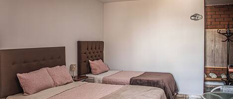 A hotel room with two beds, a small table, and a wardrobe.