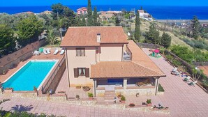 Una casa de dos pisos con piscina, un porche cubierto y vista al mar.