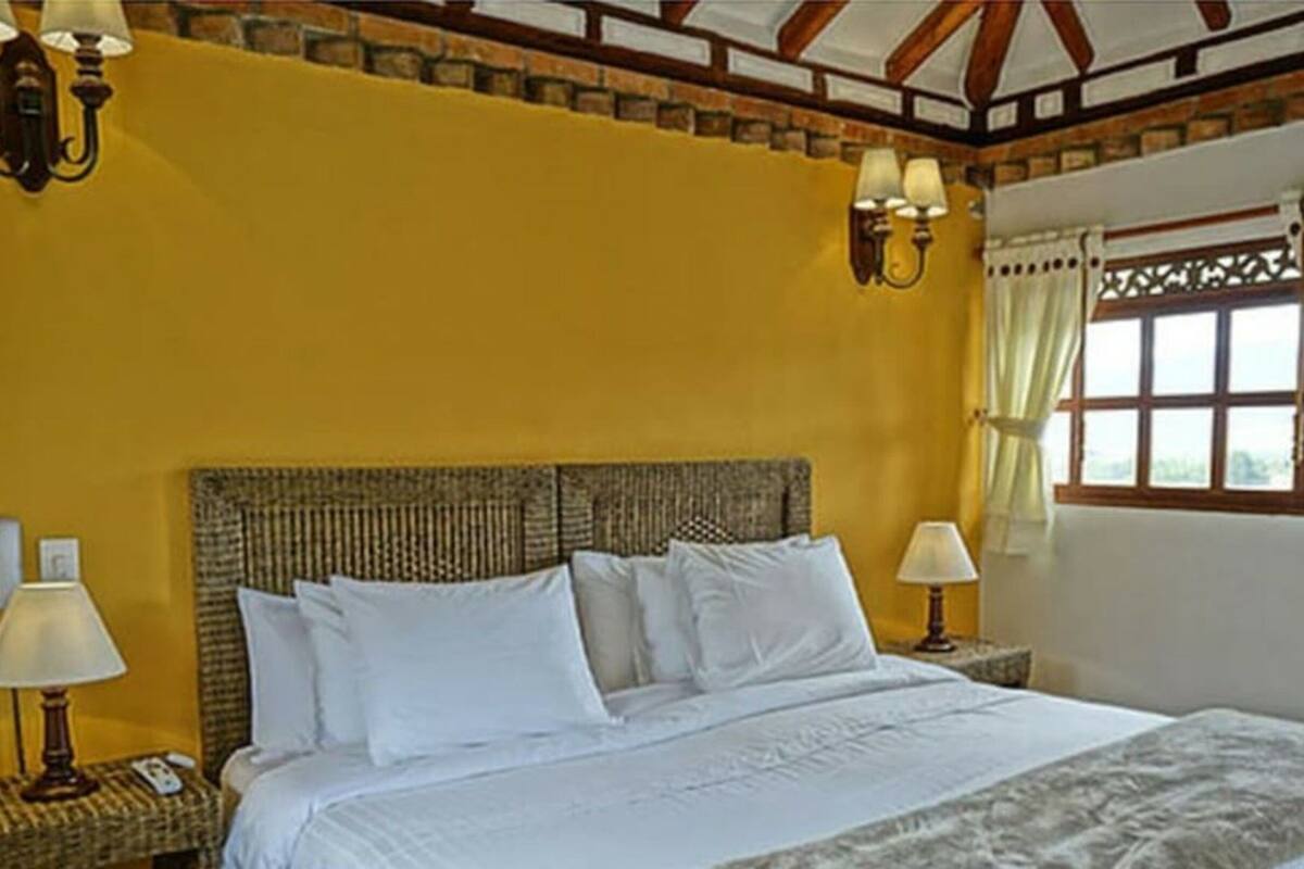 A bedroom with a large bed, two bedside tables with lamps, a window with curtains, and a brick wall.