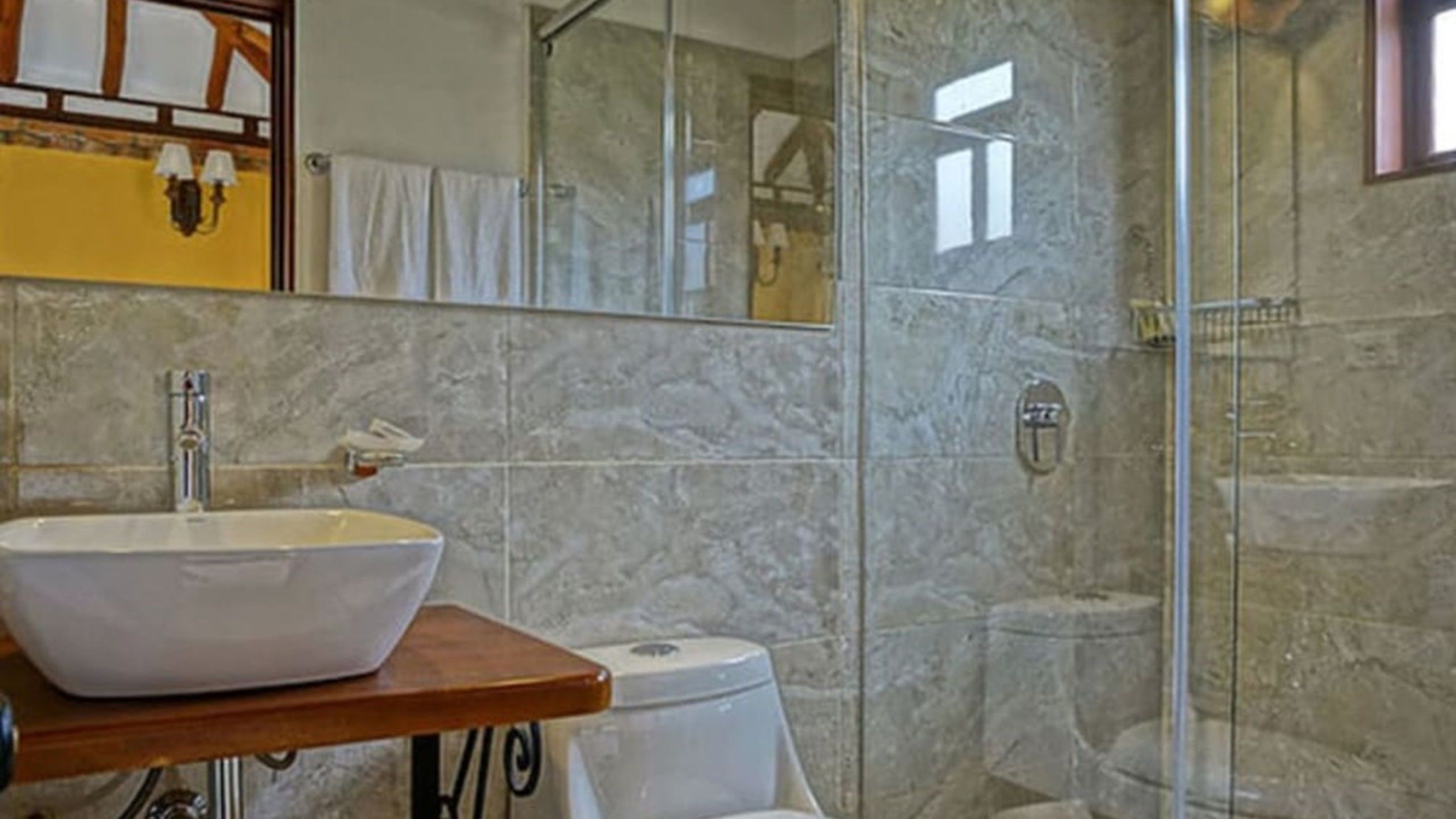Un bagno con lavabo in marmo, cabina doccia in vetro e mobile contenitore in legno.