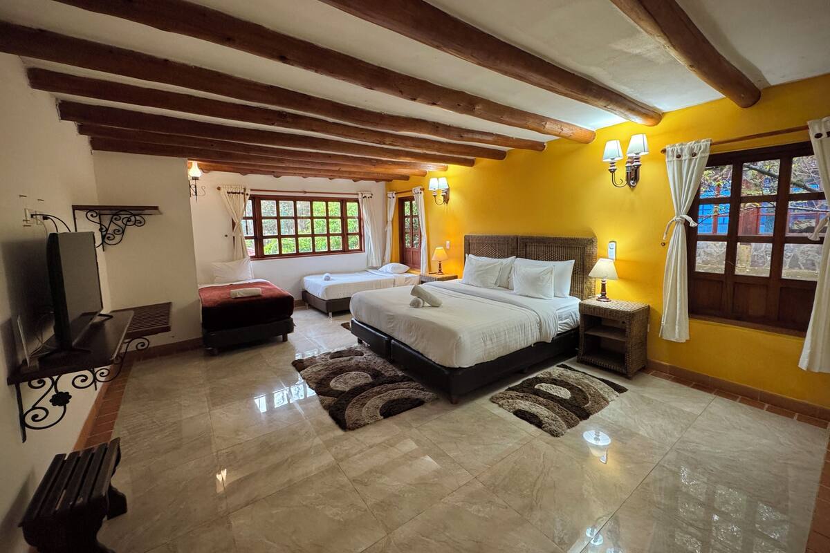 A hotel room with a large bed, two smaller beds, a TV, and a bench.