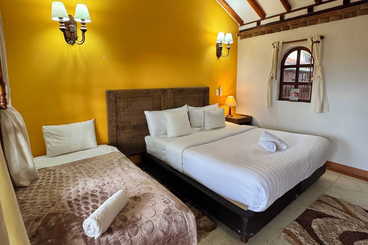 A room with two beds, wooden beams on the ceiling, and wall-mounted lamps.