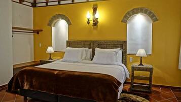 Habitación de hotel con cama, dos mesitas de noche, una lámpara de pared y una ventana con cortina.