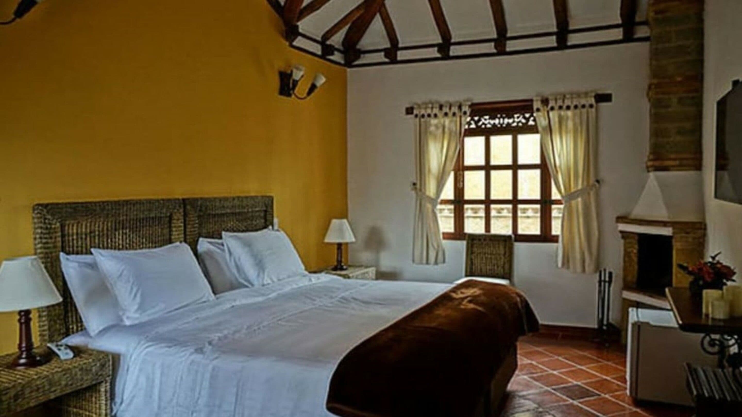 Un dormitorio con una cama grande, una chimenea y un ventanal con cortinas.