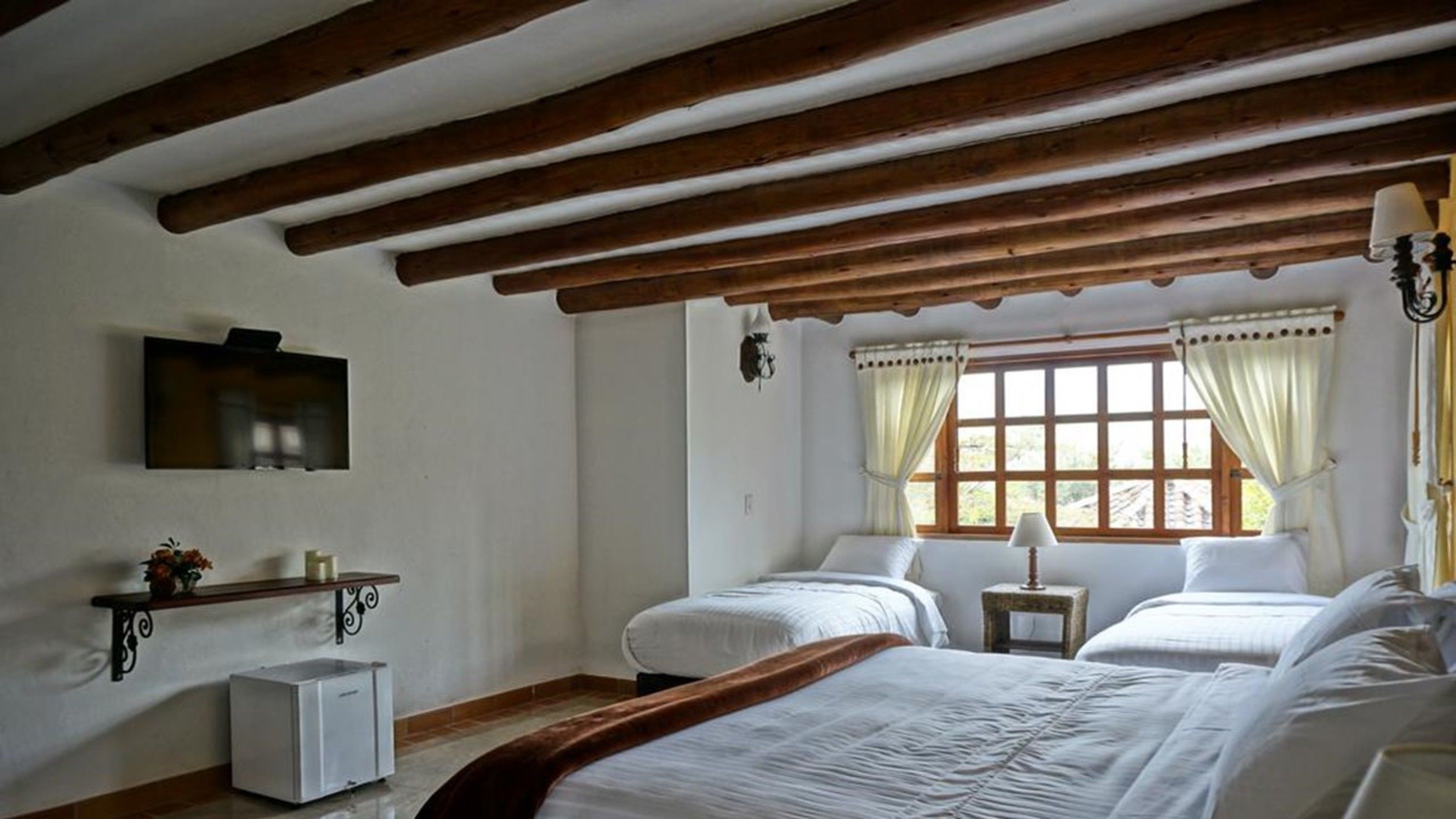 A room with two beds, a small table, a TV, and a window with curtains.