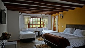 Un dormitorio con dos camas, una mesita y un ventanal con cortinas.