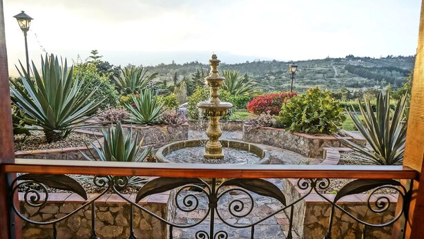 A garden with a central fountain, surrounded by various plants and a view of distant hills. - Club Campestre El Bosque de la Villa (Villa de Leyva)