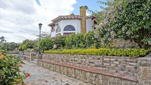 A building with a stone pathway leading to a brick wall with a bench. - Club Campestre El Bosque de la Villa (Villa de Leyva)