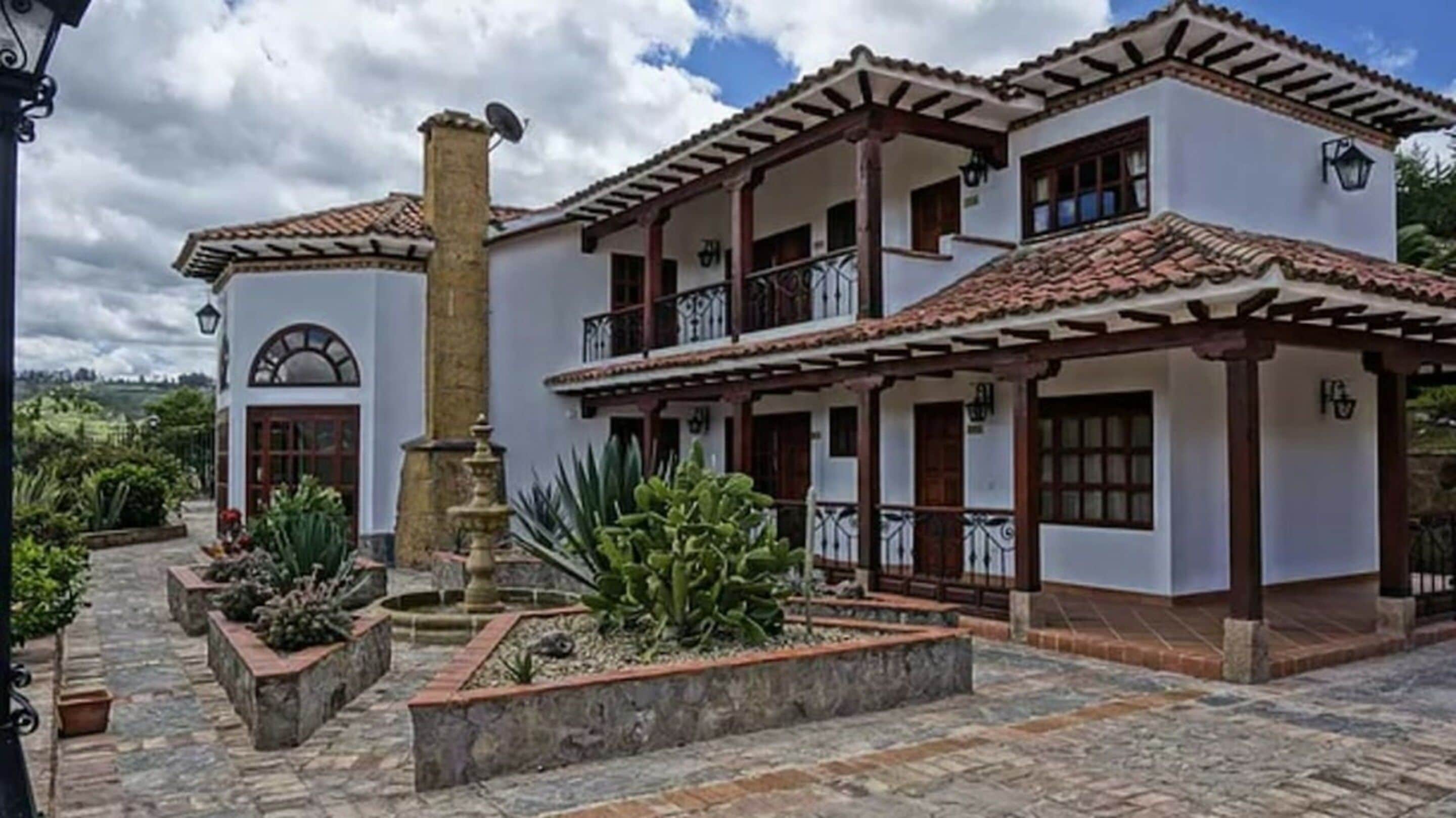 A two-story building with a tiled roof, a balcony, and a courtyard with plants and a fountain.