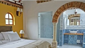 A bedroom with a bed, a nightstand, a lamp, and a view of a bathroom with a sink and mirror. - Club Campestre El Bosque de la Villa (Villa de Leyva)