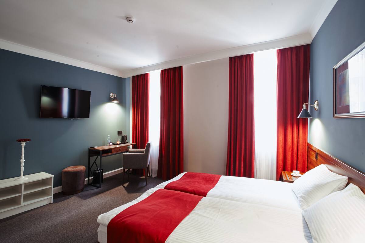 Habitación de hotel con una cama grande, un escritorio, una silla y un televisor en la pared.