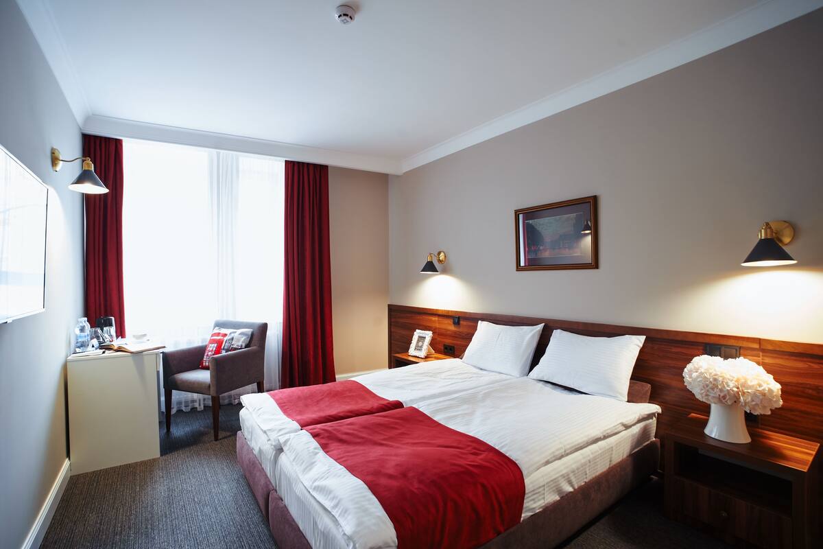 Habitación de hotel con cama, escritorio, silla y lámparas de noche.