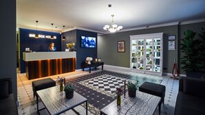 Una hall d'albergo con reception, televisore, lampadario, pavimento a scacchi e una vetrina espositiva.