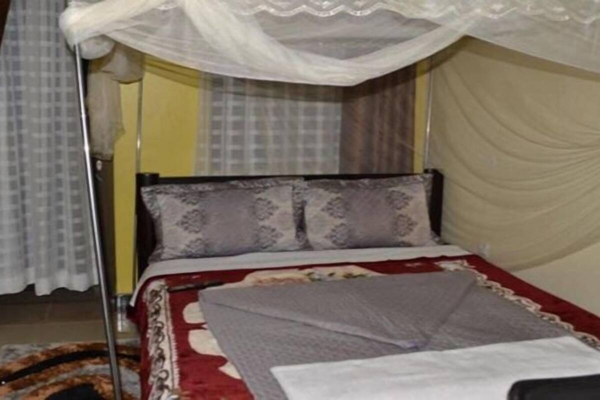 Una habitación con cama, mesita de noche, lámpara y cortina.