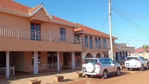 A two-story building with a balcony and a covered walkway. There are two cars parked in front. - Strikers Hotel (Soroti)