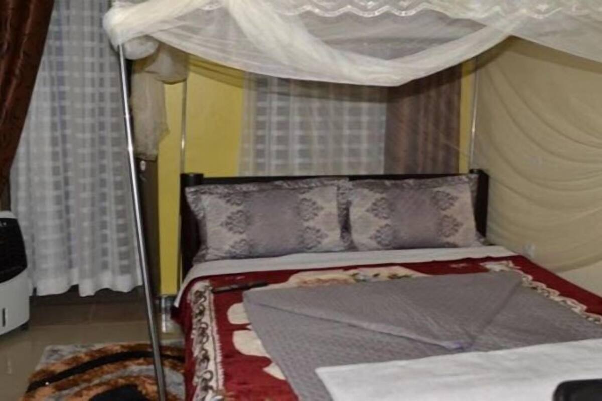Un dormitorio con una cama, una mesita de noche, una lámpara y una cortina.