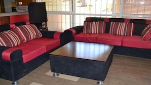 A sectional sofa with red and black cushions, a wooden coffee table, and a tiled floor. - Strikers Hotel (Soroti)