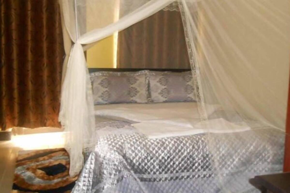 Una cama con dosel, un cojín estampado y una mesita de noche con lámpara.