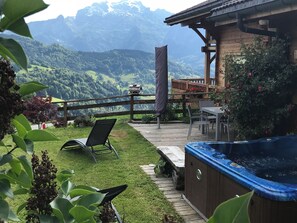 Eine Holzterrasse mit Whirlpool, Tisch und Stühlen mit Blick auf eine gebirgige Landschaft.