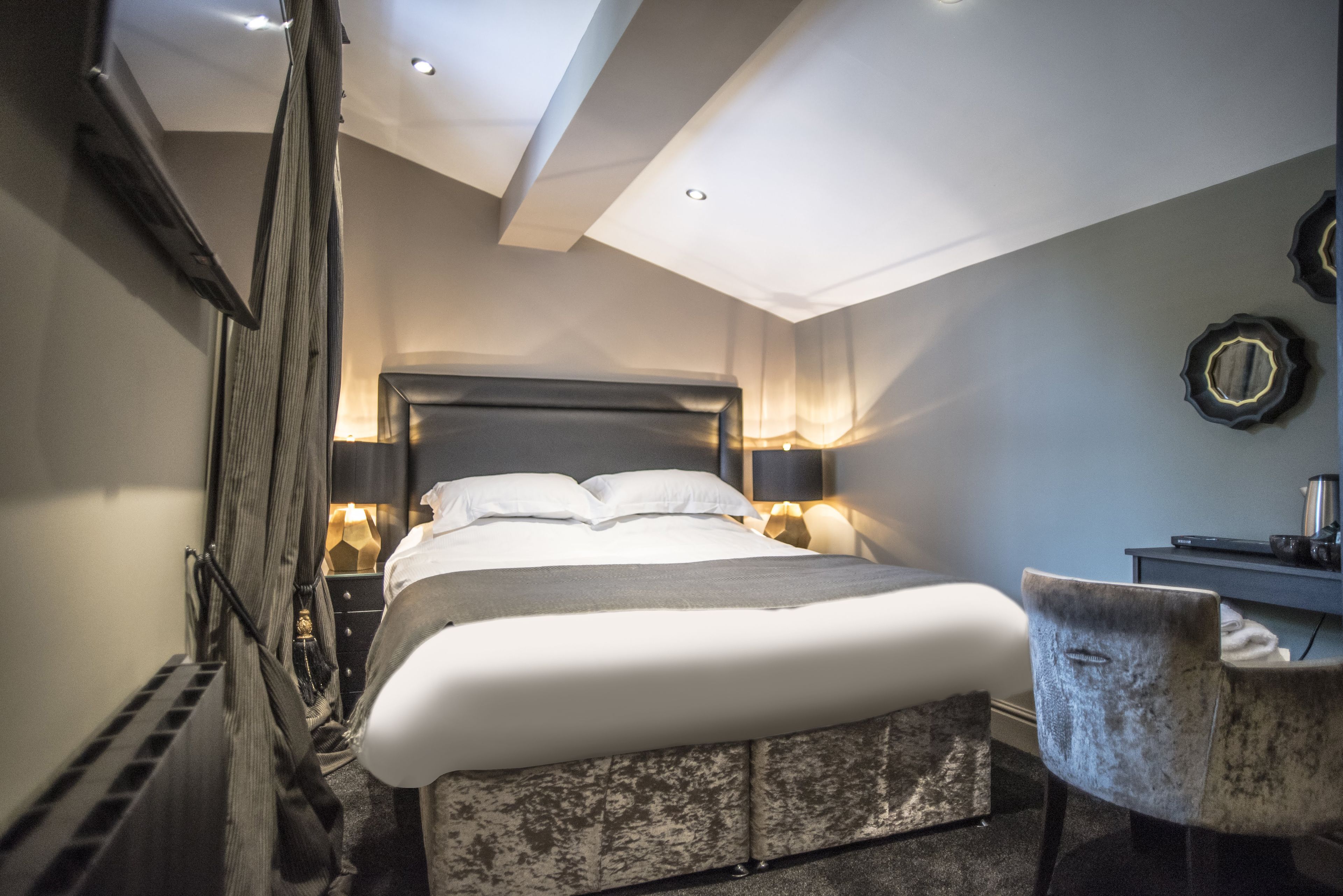 A modern hotel room with a large bed, bedside lamps, a desk, and a chair.