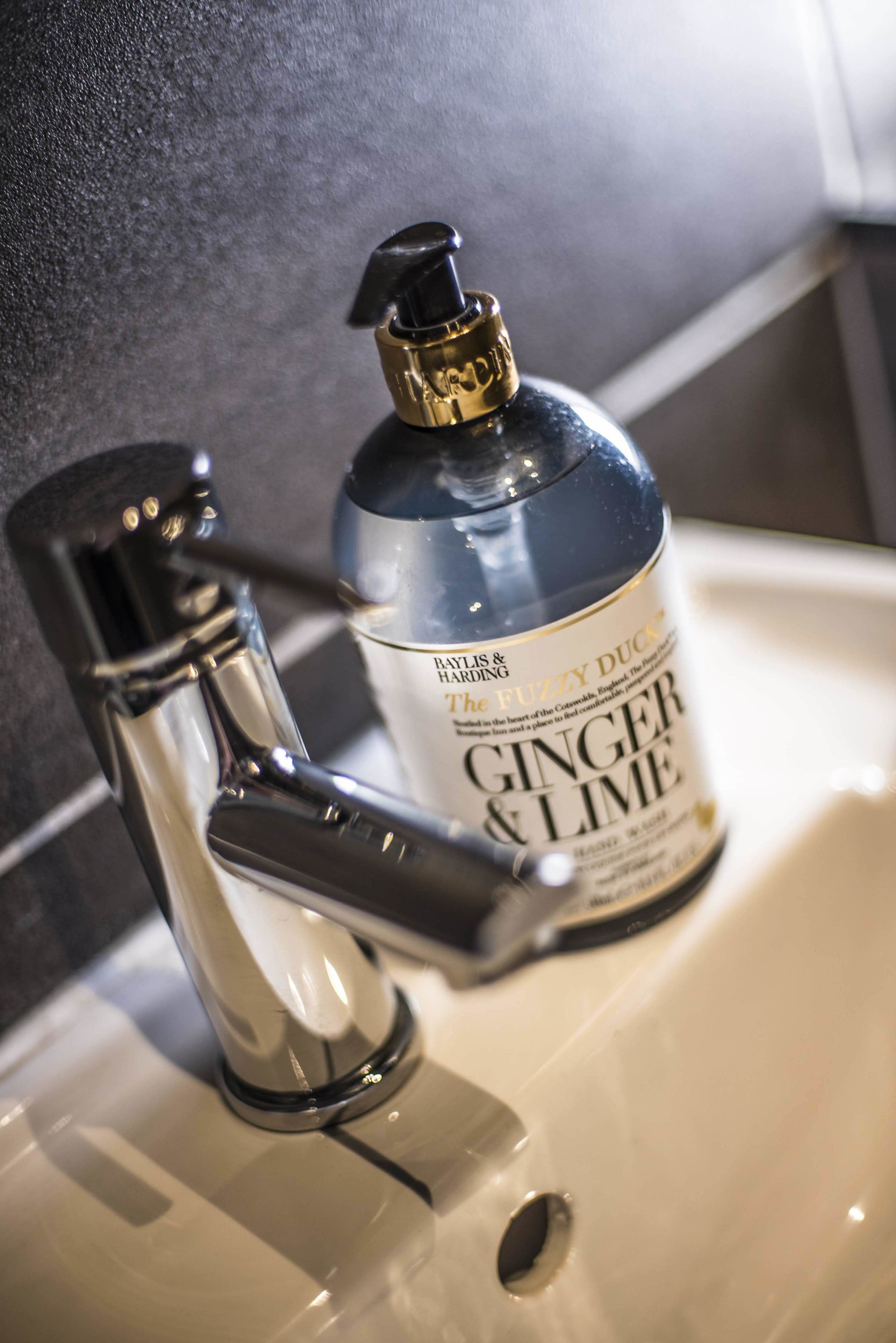 A bathroom sink with a modern faucet and a bottle of hand soap labeled "ginger & lime."