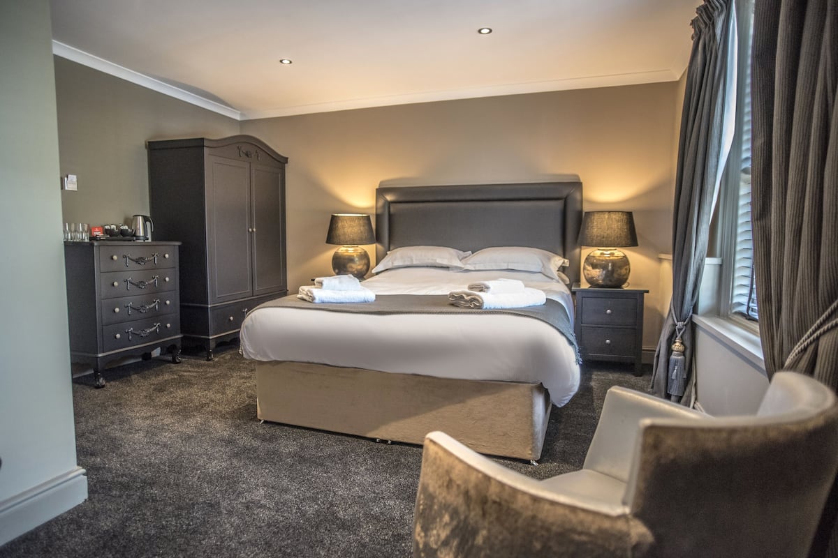 A hotel room with a large bed, a dresser, a chair, and two bedside tables with lamps.