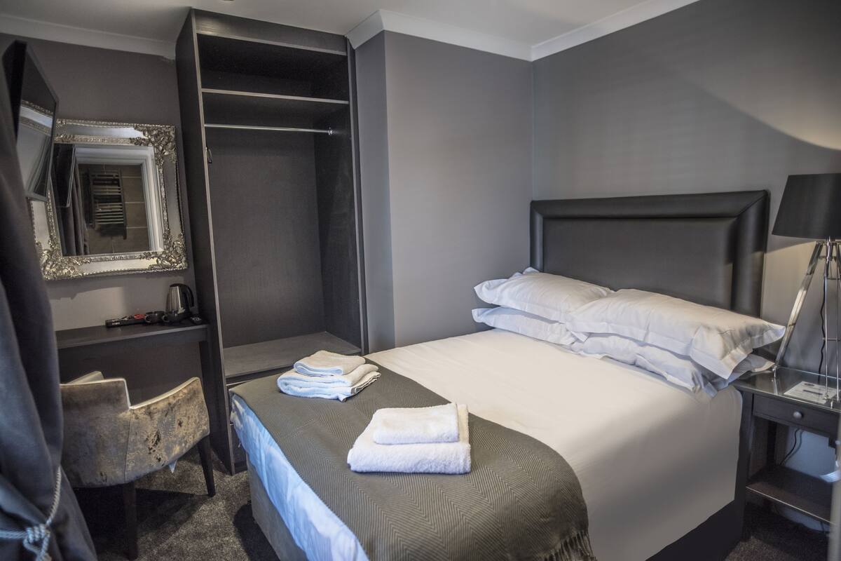 A hotel room with a bed, a desk, a chair, a wardrobe, and a mirror.