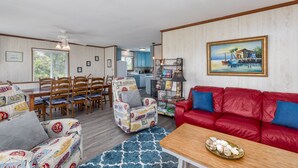 A living room with a red sofa, patterned armchairs, a wooden coffee table, and a dining area with wooden chairs and a table. - 4752- Canopy Retreat, Walk to Beach | Quiet Kitty Hawk Retreat (Kitty Hawk)