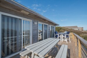 A wooden deck with a table and chairs, large sliding glass doors, and a view of the beach. - 4752- Canopy Retreat, Walk to Beach | Quiet Kitty Hawk Retreat (Kitty Hawk)