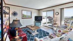 A living room with a television, a red sofa, a wooden coffee table, and a patterned armchair. - 4752- Canopy Retreat, Walk to Beach | Quiet Kitty Hawk Retreat (Kitty Hawk)