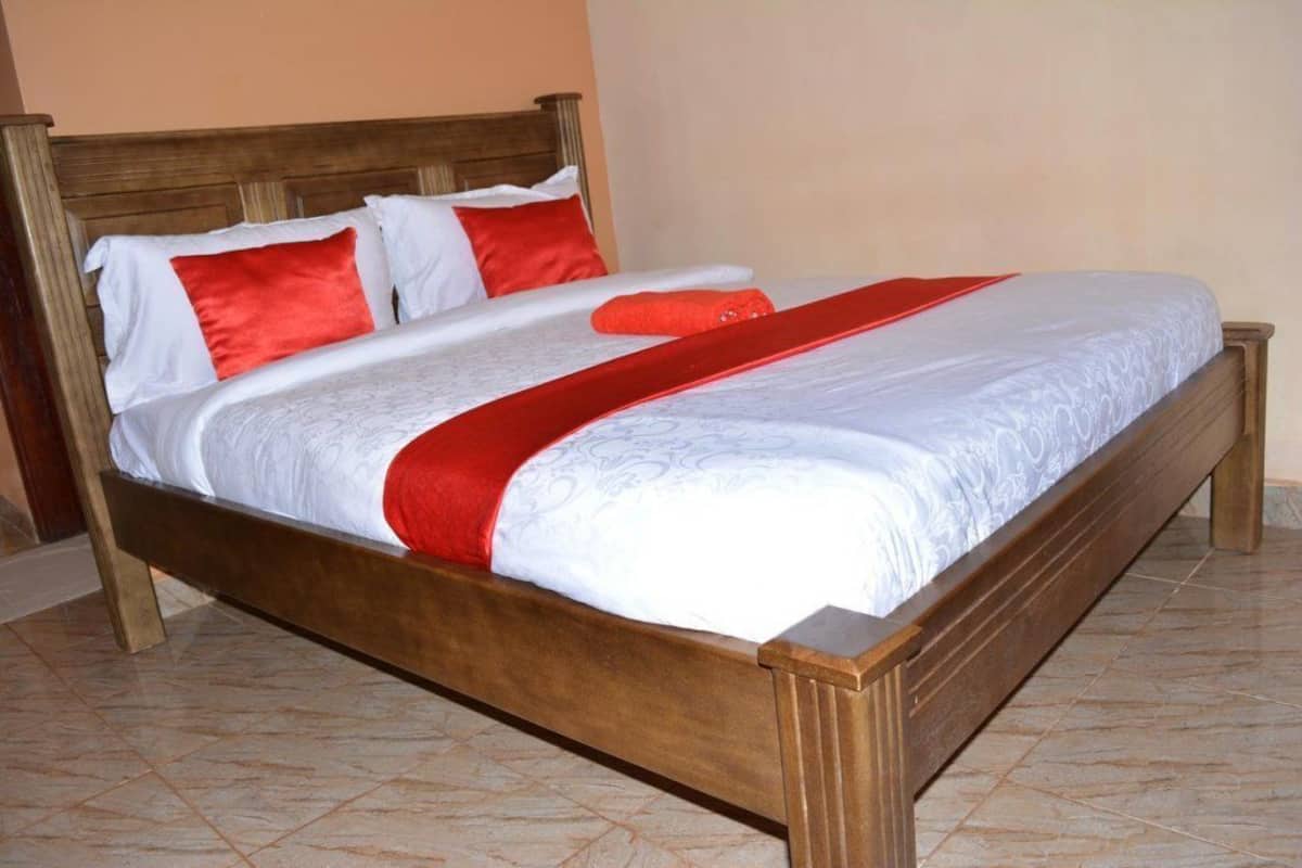 A bed with a wooden frame, white bedding, and red accents.