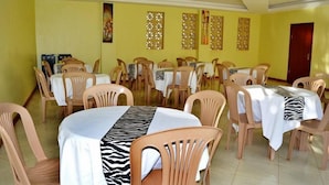 A dining area with multiple tables and chairs, yellow walls, and decorative panels. - Mak Cottages (Kampala)