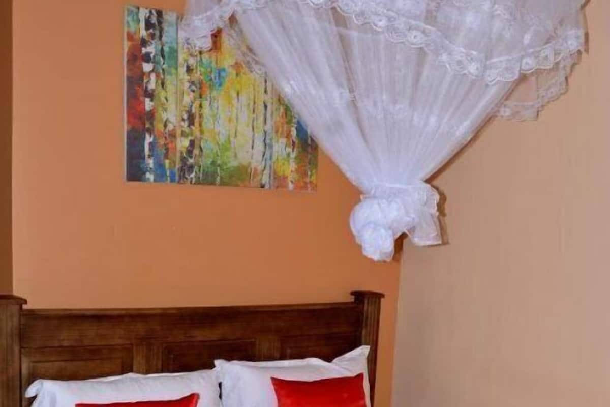 A bed with a wooden headboard, white bedding with red accents, and a colorful abstract painting on the wall.