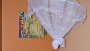A bed with white bedding and red accents, a wooden headboard, and a colorful abstract painting on the wall. - Mak Cottages (Kampala)