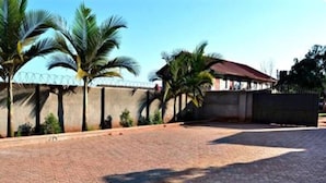 A paved courtyard with palm trees and a building with a red roof. - Mak Cottages (Kampala)