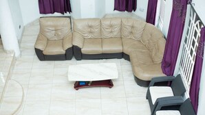 Un sofà seccional beix amb un otomà a joc en una habitació amb terra de rajola i cortines morades.