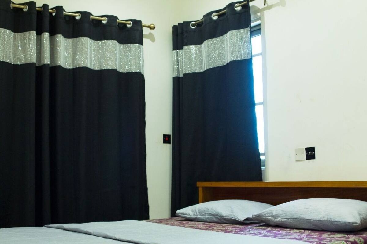 A bedroom with a bed, two pillows, and black curtains with silver trim.