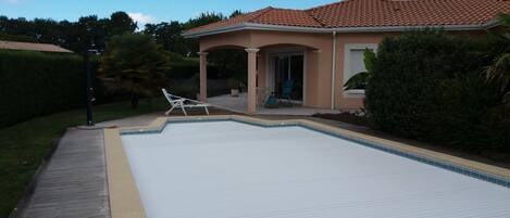 A swimming pool with a wooden deck, two lounge chairs, and a covered patio area.