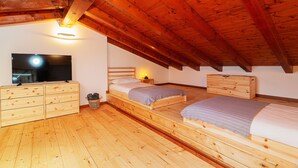 A wooden attic bedroom with two beds, a TV, and a dresser. - Panoramic View of Lake Maggiore Near Stresa • Private Garden & Parking (Levo di Stresa)